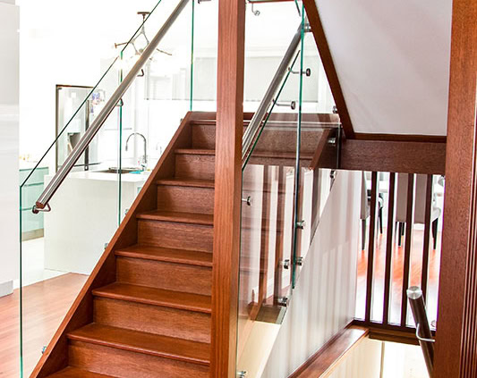 Modern wooden staircase with glass and metal handrails in a residential interior.