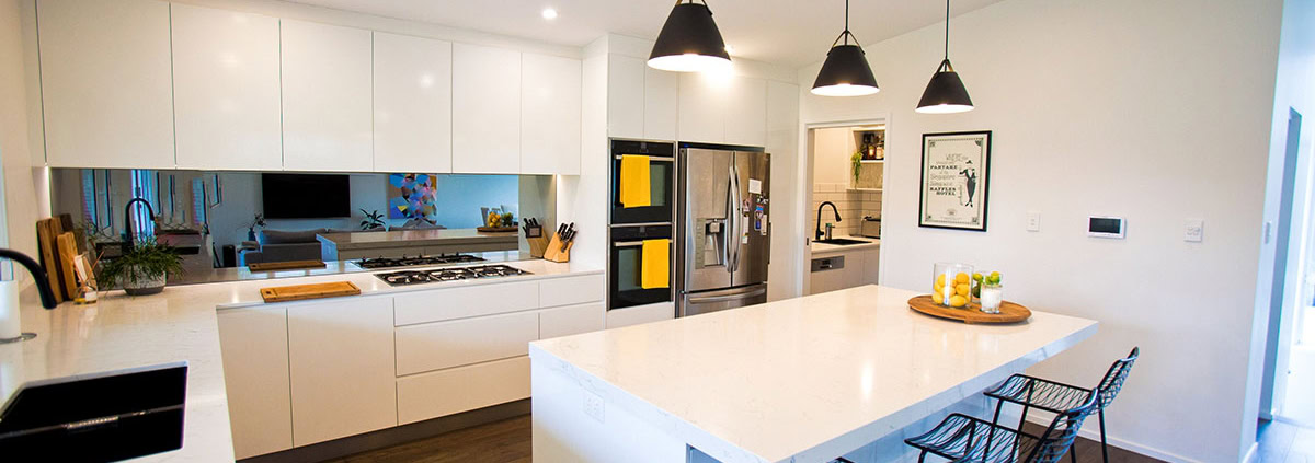 Bright, contemporary kitchen with white cabinetry, island, and black pendant lights in Sydney home.