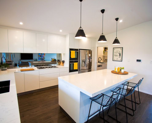 Bright, contemporary kitchen with white cabinetry, island, and black pendant lights in Sydney home.