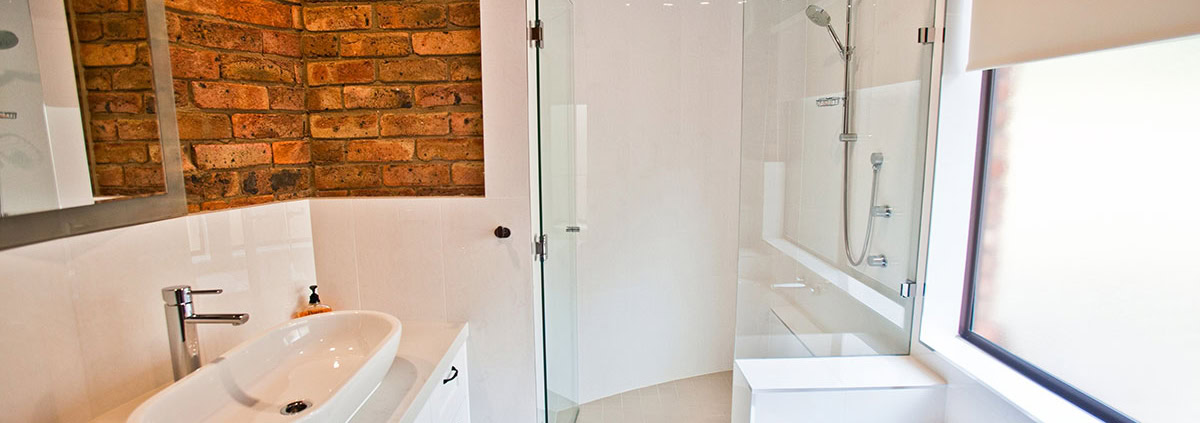 Bright bathroom with brick wall, white fixtures, and a large window in a Sydney home renovation.