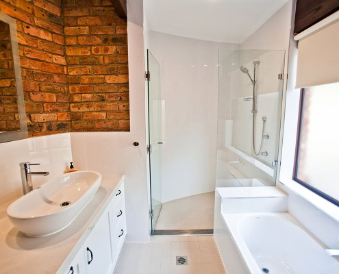Bright bathroom with brick wall, white fixtures, and a large window in a Sydney home renovation.
