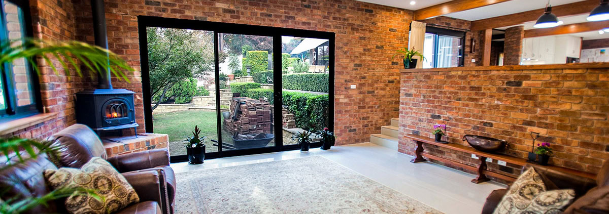 Modern living room with brick walls, large glass doors, and cozy furniture in Sydney home.