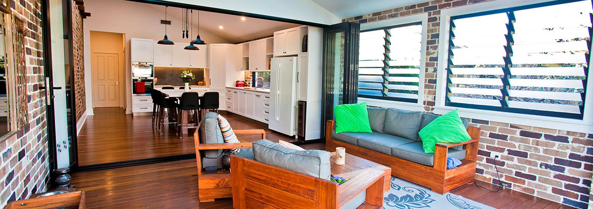 Spacious living room with brick walls, wooden floors, and large louvered windows in a Sydney home.