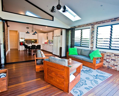 Spacious living room with brick walls, wooden floors, and large louvered windows in a Sydney home.