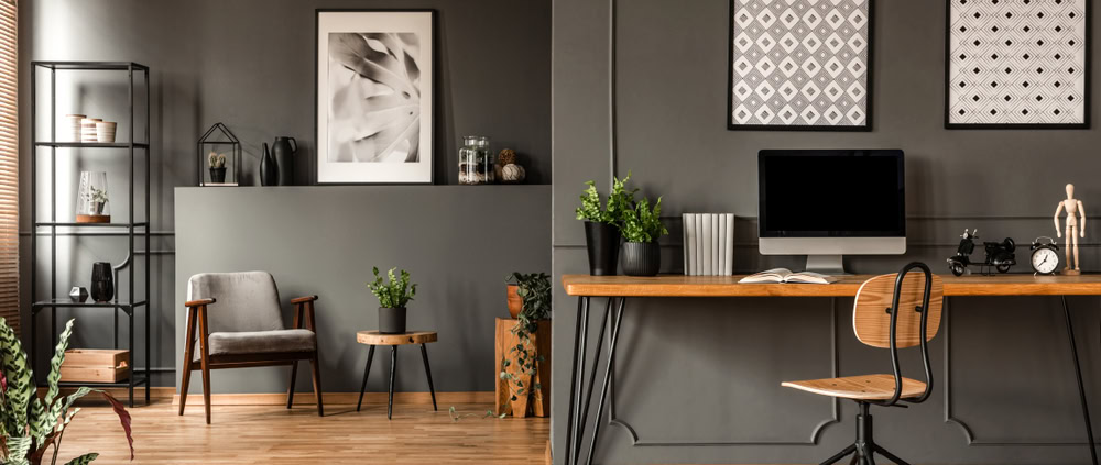 Interior of a stylish home office with grey walls, a wooden desk, and decorative artwork.