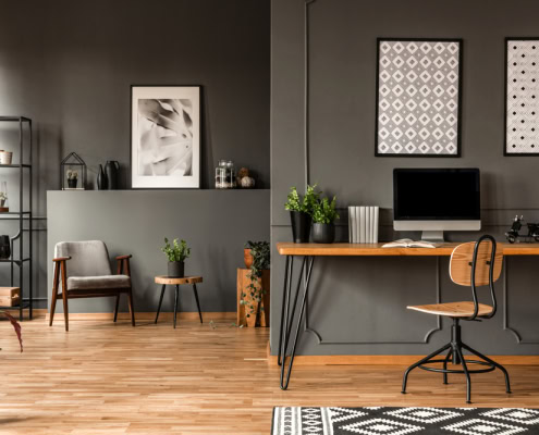 Interior of a stylish home office with grey walls, a wooden desk, and decorative artwork.