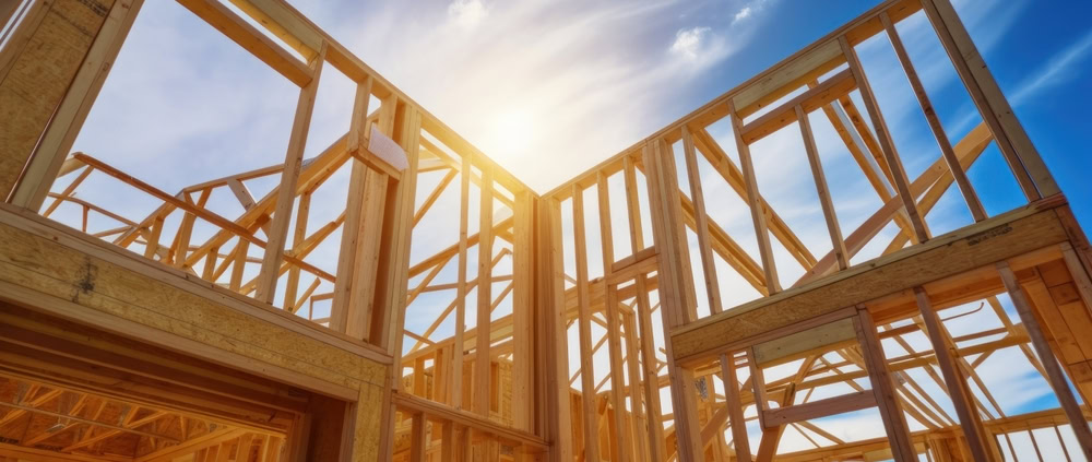 Wooden house frame under construction with blue sky and sunlight.