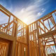 Wooden house frame under construction with blue sky and sunlight.