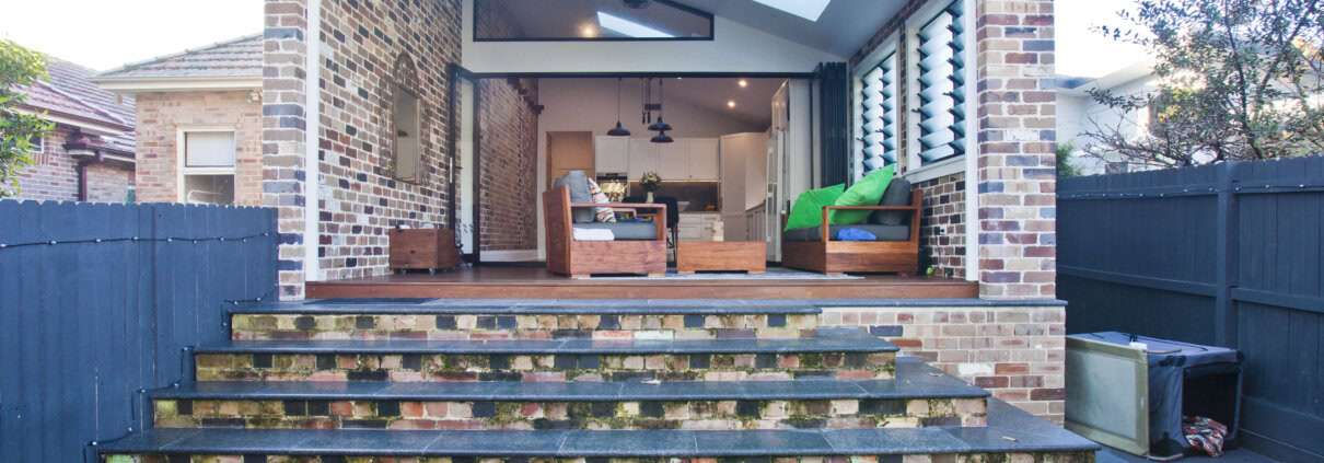 Outdoor living area with brick walls, wooden steps, and contemporary furniture in a residential back.