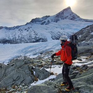 Mountain climber in red gear on glacier with mountain peak in background.