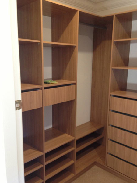 Walk-in wardrobe with wooden shelves, drawers, and storage compartments in Sydney.