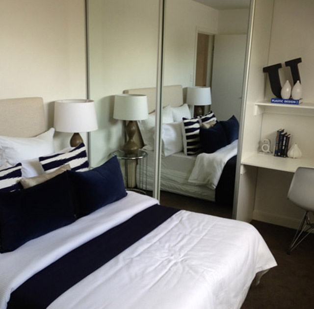 Contemporary bedroom featuring a wardrobe with mirrored sliding doors, navy bedding, and modern deco.