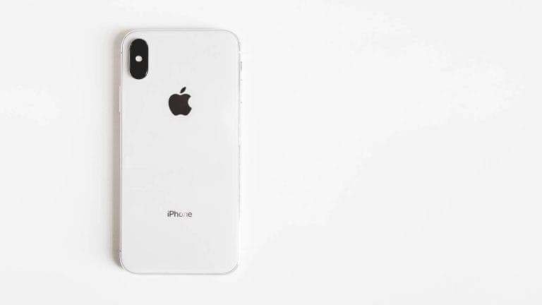 The back of a white and silver iPhone X lying on a plain white background.