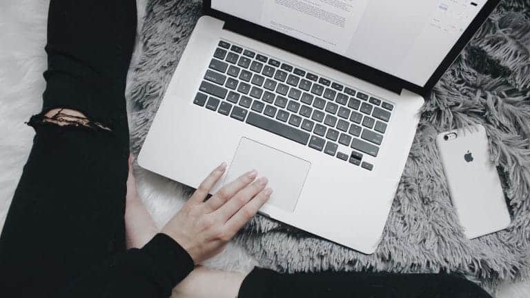 Top-down view of a person sitting on a shaggy grey rug using a laptop, with a smartphone nearby.
