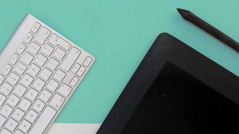 Top-down view of a graphics tablet, stylus, and keyboard on a teal and white background.