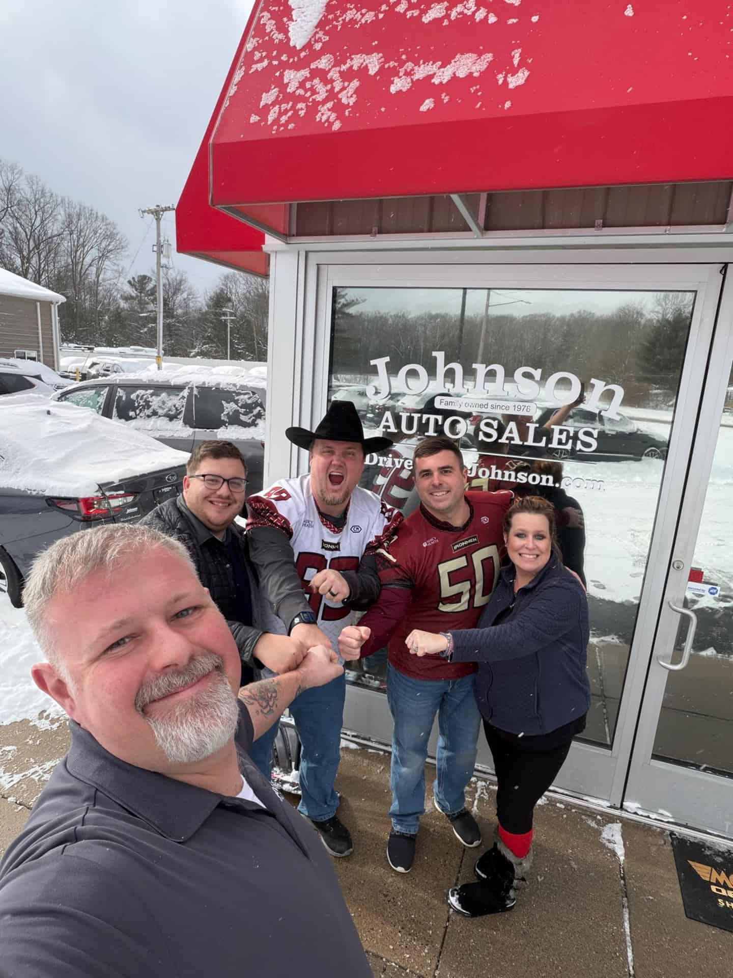 Group of people standing outside Johnson Auto Sales in winter.