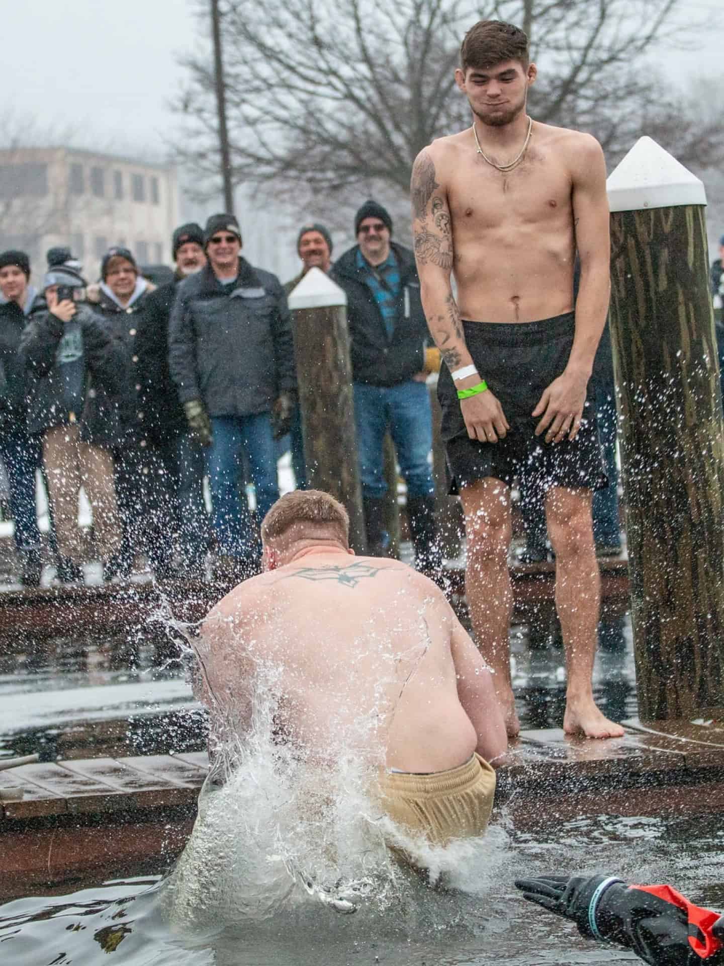 Two young men by the water with spectators watching in the background.
