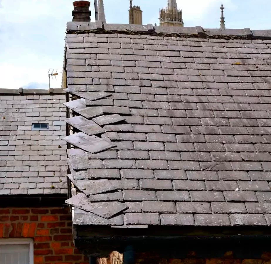 Storm Damage 4 A slate roof with several loose, overlapping tiles near the edge—some sticking up and misaligned—shows clear need for storm damage roof repair.