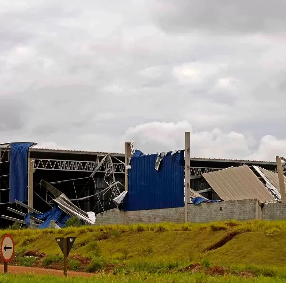 Storm Damage 9 A large industrial building with a blue metal roof is severely damaged, with collapsed sections and debris scattered around, highlighting the urgent need for emergency storm damage repair under a cloudy sky.