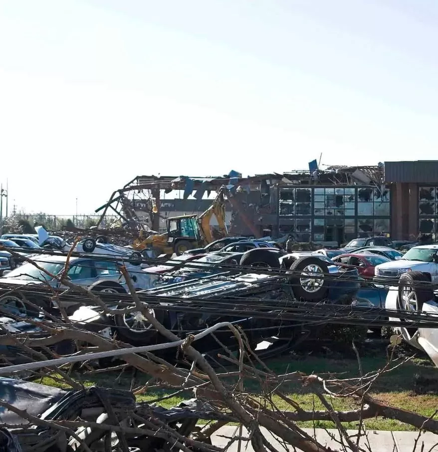 Storm Damage 10 Damaged cars and debris cover the ground with a partially destroyed building and construction equipment visible in the background, highlighting the urgent need for storm damage repair.