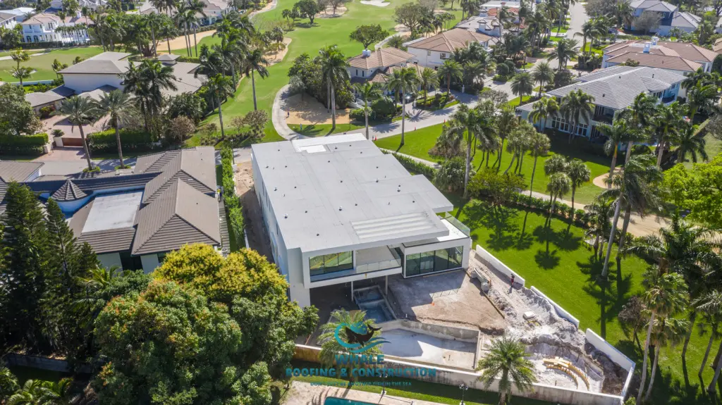 Flat Roof 1 Aerial view of a modern house with a flat roof under construction, featuring an unfinished backyard and pool in a residential neighborhood with a golf course nearby.