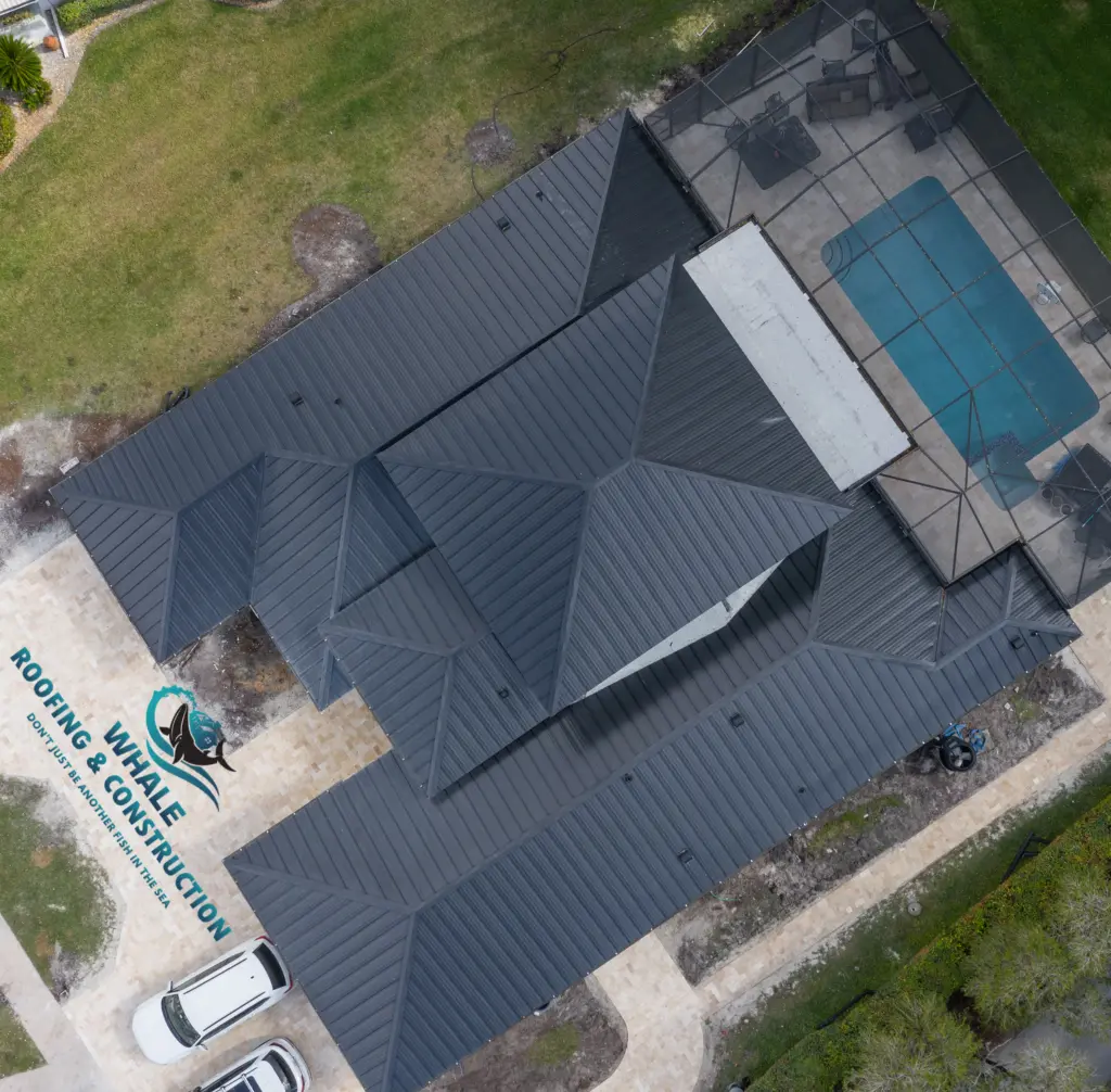 Metal Roof Replacement in Parkland 3 Aerial view of a house with a dark metal roof, screened pool area, two white vehicles parked outside, and Whale Roofing & Construction logo in the bottom left corner.