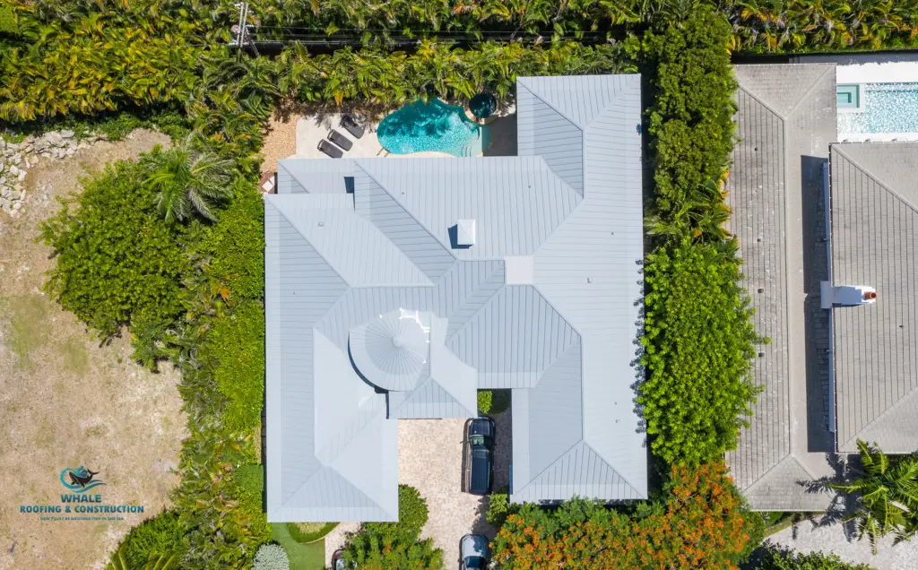 Metal Roofing Contractors 3 Aerial view of a house with a metal roof, central driveway, two parked vehicles, swimming pool in the backyard, and surrounding greenery.