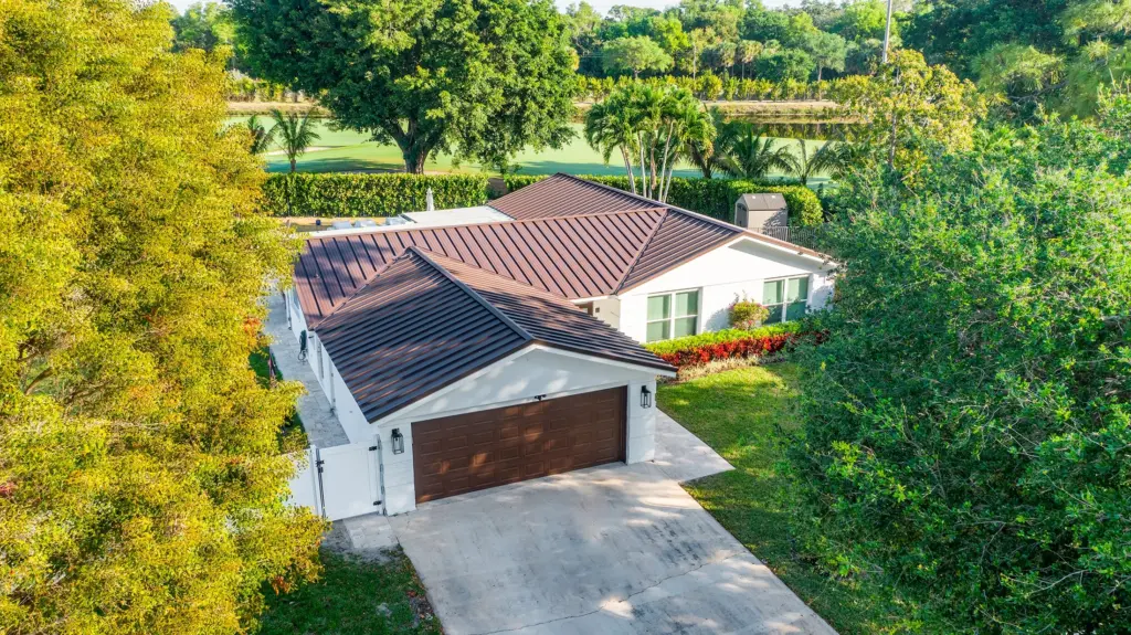 Aerial view of a single-story house with a dark brown roof, white exterior, and double garage, surrounded by trees and greenery—showcasing the quality often delivered by Palm Beach County roofing companies.