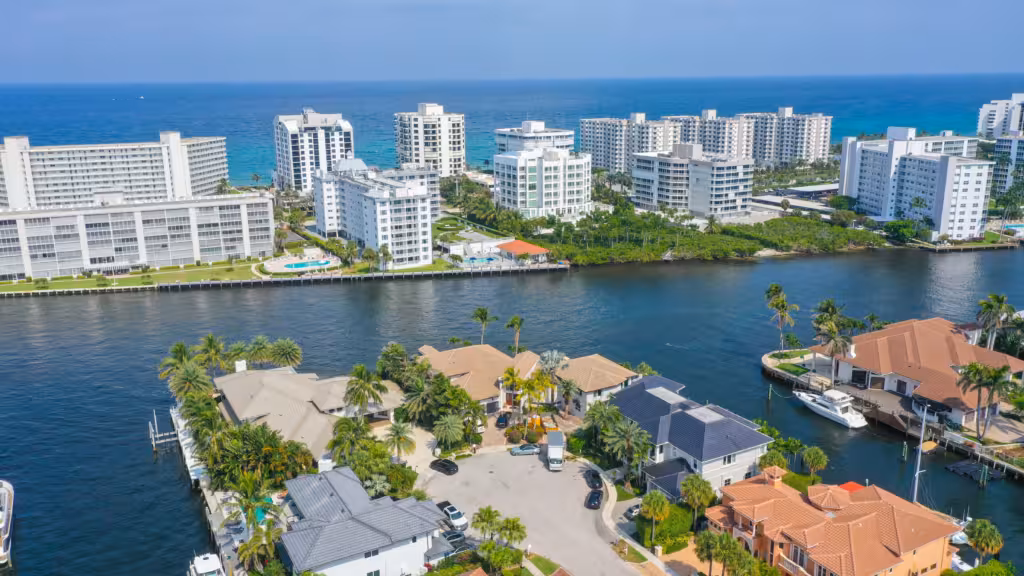 Tile Roofing 3 Aerial view of waterfront homes with stunning tile roofs and high-rise condominiums separated by a canal, the ocean visible in the background under a clear blue sky—showcasing craftsmanship from a leading tile roofing company.