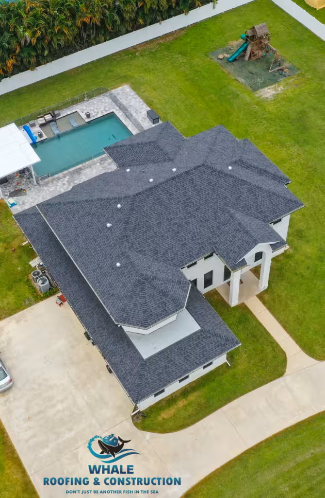 Shingle Roofing 2 Aerial view of a large house with a dark shingle roof, backyard pool, playset, and neatly maintained lawn. Whale Roofing & Construction logo is visible on the driveway.