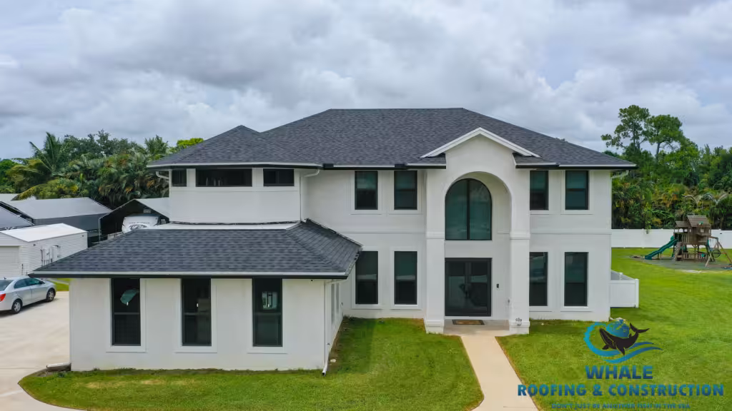 Two-story modern house with dark shingle roof, white exterior walls, and large front windows. The logo for Whale Roofing & Construction is visible in the bottom right corner.