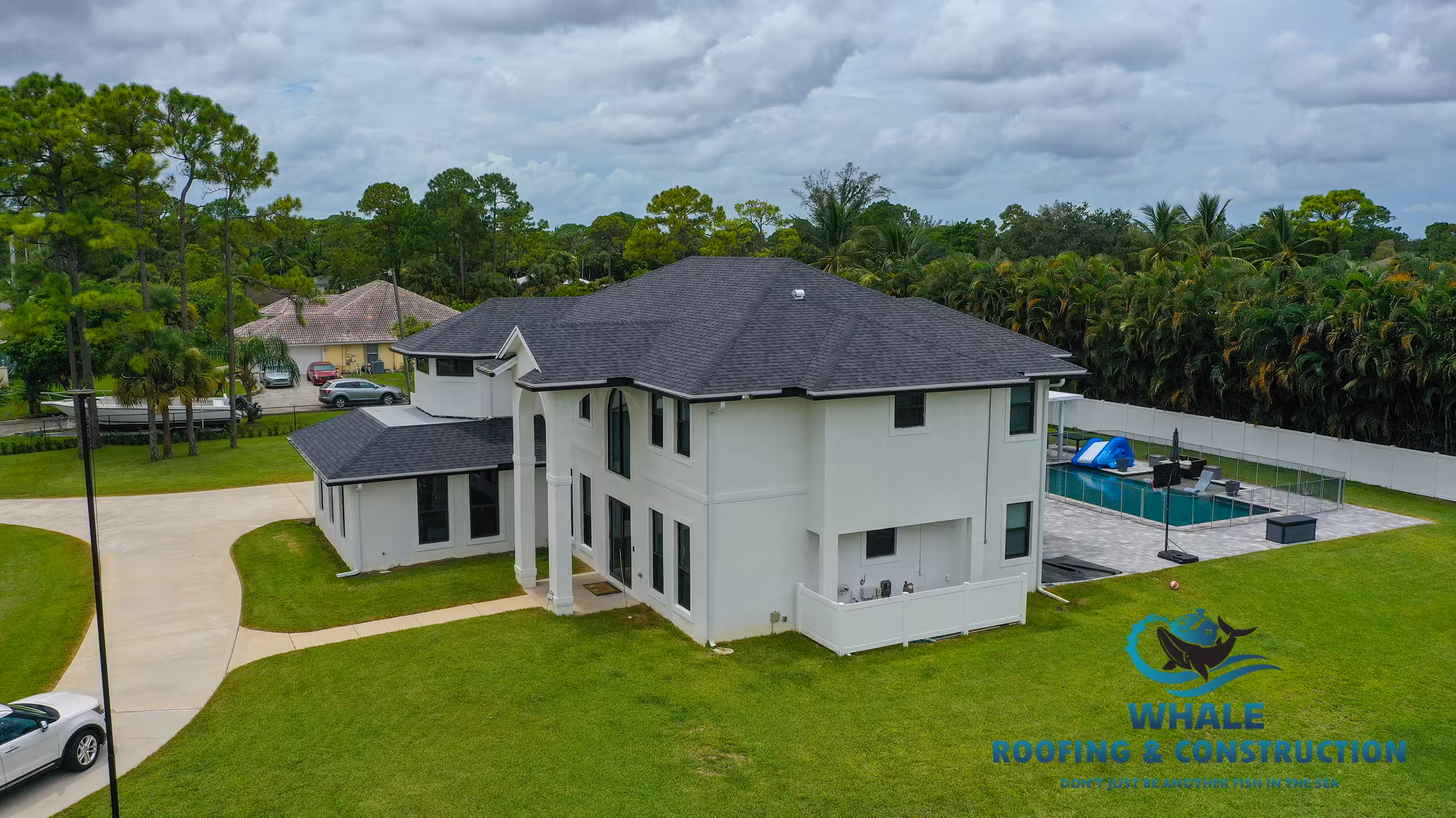 A two-story white house with a dark gray roof, large backyard, swimming pool, and driveway, surrounded by trees and grass. "Whale Roofing & Construction" logo in the bottom right corner.