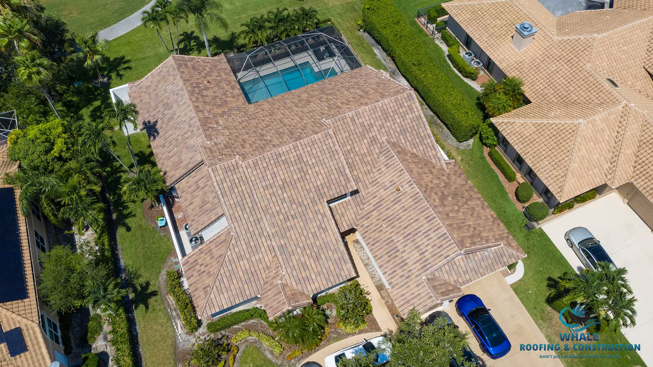 Aerial view of a large house with a brown shingle roof, screened pool area, driveway, and surrounding greenery in a residential neighborhood.