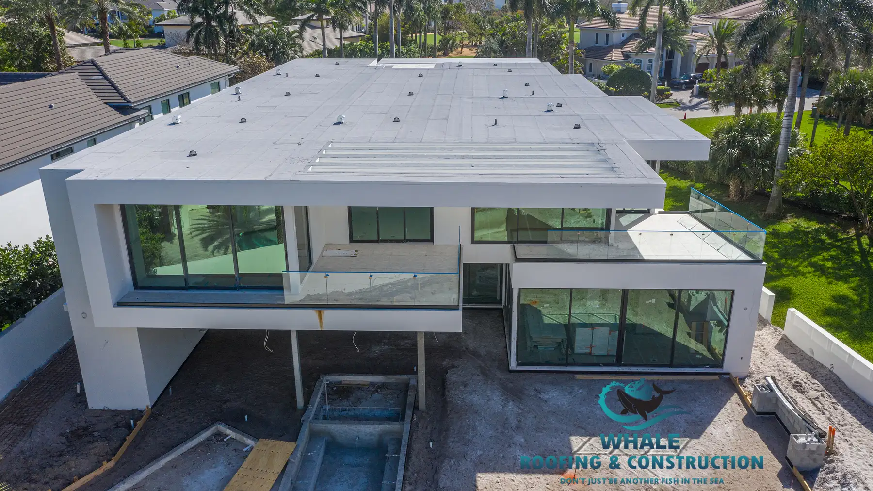 A modern two-story house under construction featuring large glass windows, balconies, and an unfinished pool, with the Whale Roofing & Construction logo in the foreground.