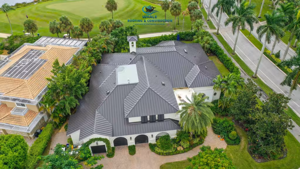 A Brief Look At The Top 12 Most Common Roofing Issues in South Florida—and How to Fix Them 2 Aerial view of a large house with a dark gray metal roof, surrounded by palm trees and greenery, near a road and golf course.