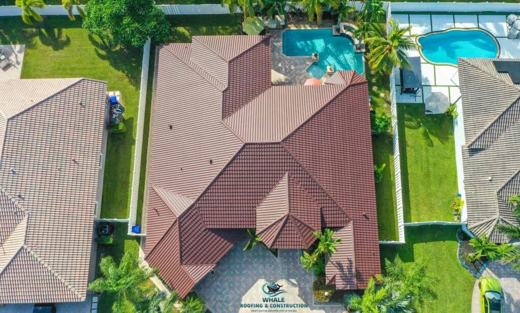 Aerial view of a house with a brown tiled roof, surrounded by a lawn, palm trees, and a backyard pool; neighboring houses and fences are visible.