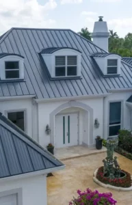 A modern house with a dark metal roof, white exterior walls, large windows, and a double-door entrance is surrounded by plants and a circular flower bed with a statue—ideal for those seeking expert roof maintenance Boca Raton services.