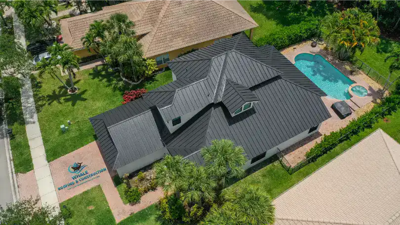 Roofing Trends That South Florida Homeowners Can't Ignore in 2025 1 Aerial view of a house with a dark metal roof, a 2025 roofing trend in South Florida, surrounded by green lawns, palm trees, and a backyard pool.