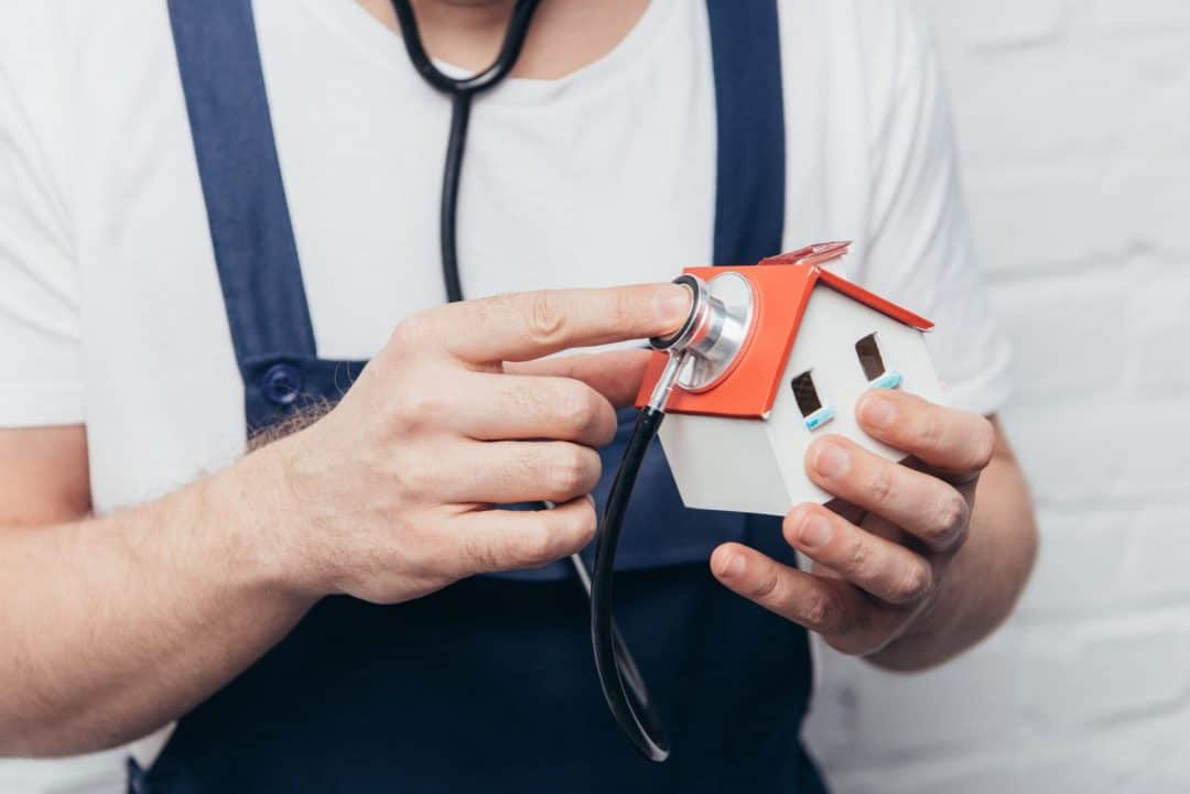 cropped shot of craftsman checking house figure by stethoscope, home inspection concept a man in overalls using a stethoscope checking the top of a roof illustrating roof inspections.