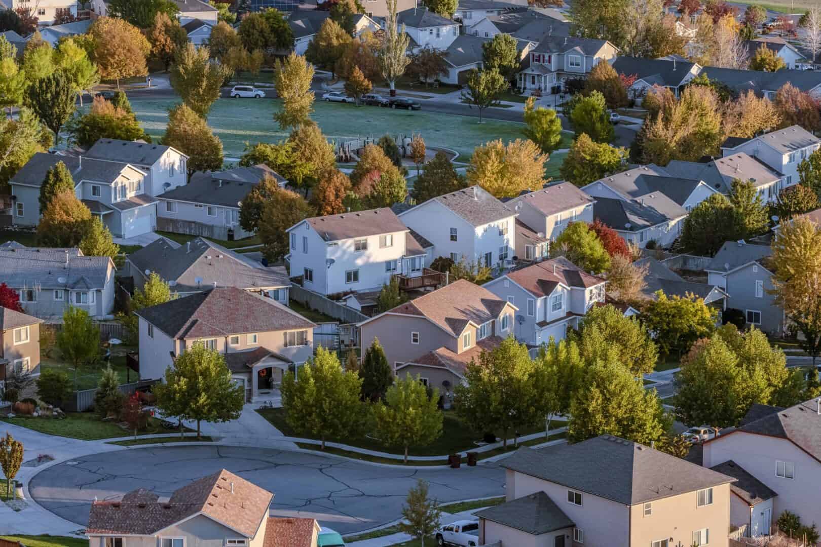 Aerial view of Calgary suburban homes with a mix of roof styles and materials surrounded by autumn trees