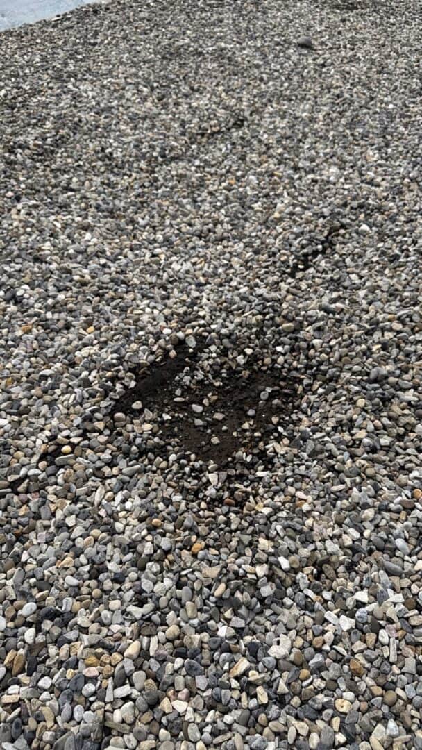 Close-up of a gravel flat roof in Calgary showing a dark, sunken area where the membrane may have failed—suggesting water penetration from a popped seam beneath the surface.