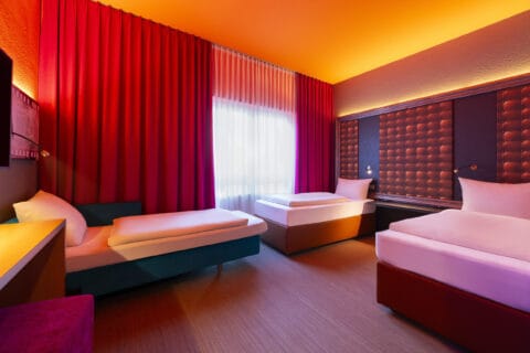 Behindertengerechtes Zimmer – zwei elektrisch verstellbare Einzelbetten mit viel Abstand. Schlafsofa, Regal als Nachttisch zwischen den Betten und wandmontierte, schwenkbare Lampen.