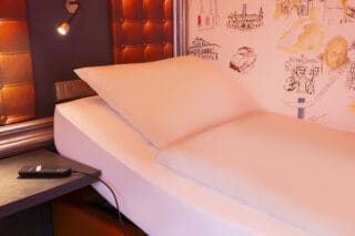Behindertengerechtes Zimmer – elektrisch verstellbares Einzelbett mit Fernbedienung. Nachttisch neben dem Bett und wandmontierte, schwenkbare Lampen.
