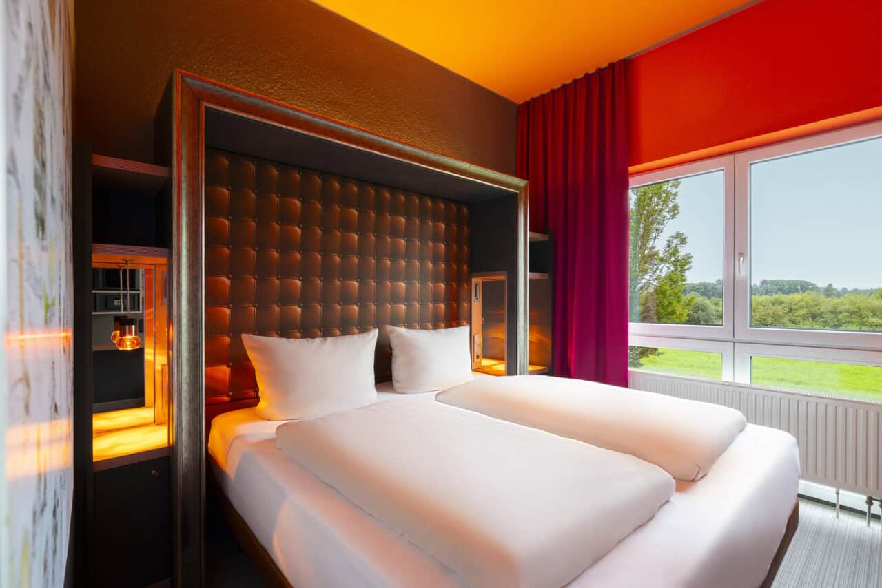 Hotel room view with view of the bed and window behind it, with open curtains and view of the landscape conservation area.