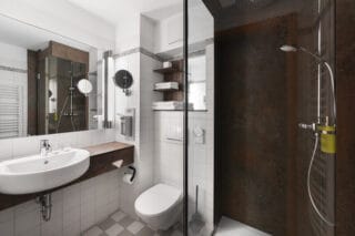 Badezimmer: Ebenerdige Dusche mit ausklappbarer Sitzfläche und Glastüren, Waschtisch mit Aufsatzwaschbecken, Wandspiegel, Kosmetikspiegel, Handtuchregal, WC, Föhn, Wandheizung