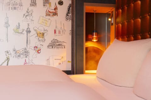 Zimmer- Detailansicht vom Bett mit Hannover Foto-Tapete, Nachttischlampe leuchtet