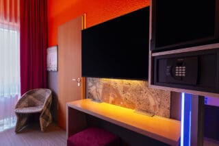 Zimmer – Blick zur Verbindungstür und Arbeitsplatz. Schreibtisch, TV/Safe/Minibar in Augenhöhe, Kommode
