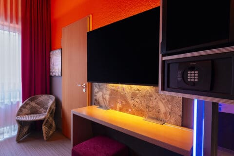 Zimmer – Blick zur Verbindungstür und Arbeitsplatz. Schreibtisch, TV/Safe/Minibar in Augenhöhe, Kommode