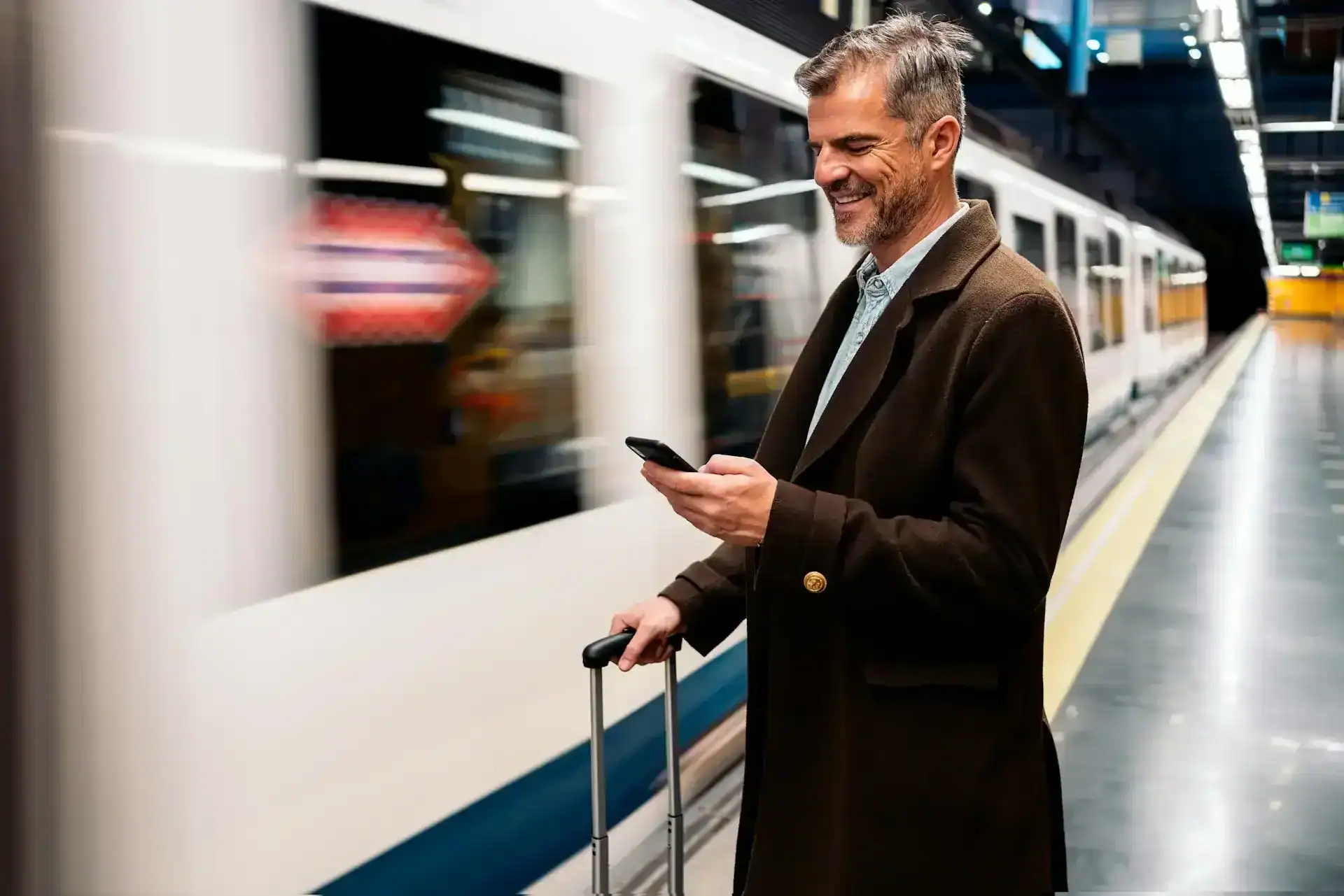 Reisende Person checkt per Smartphone am Bahnsteig ins Hotel ein, Rollkoffer neben sich.