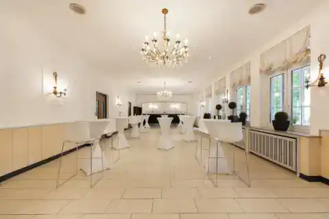 Conference room IX (bistro) - frontal perspective. Bar tables with bar stools in a row, two chandeliers, wall lights on all walls, window front on the right with curtains and plant decoration, tiled floor
